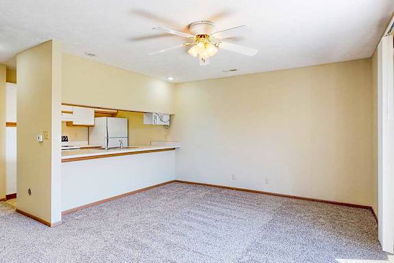 A living area with a ceiling fan and a view of the kitchen.
