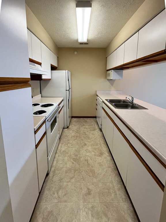 a galley kitchen with white appliances and brown trim