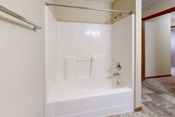 A bathroom with a combination shower and tub, with a curtain rod and a towel rack.