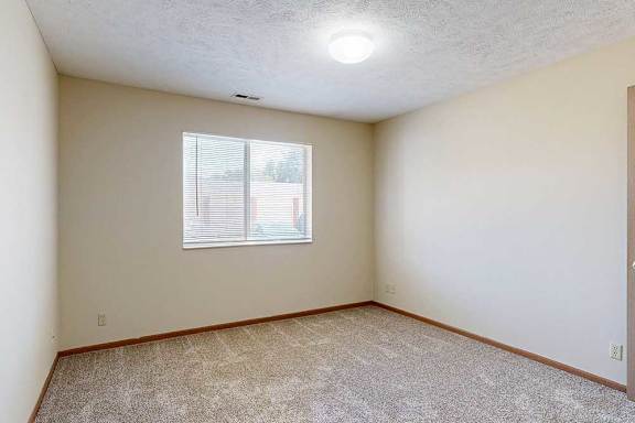 A bedroom with a window and carpeted floor.