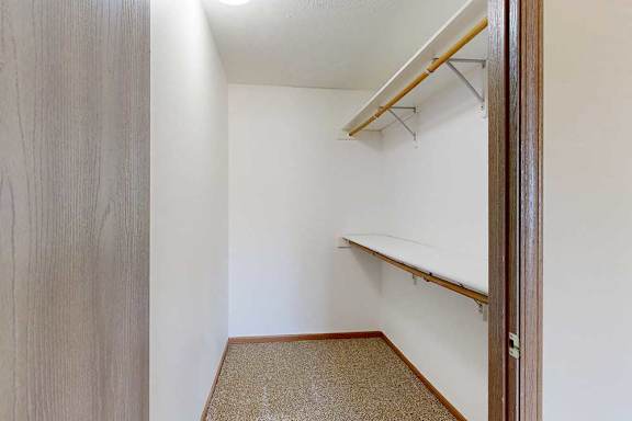 A long walk-in closet with two built-in shelves and hanging space to the right.