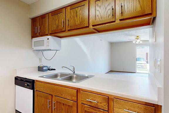 A kitchen with wooden cabinets and a passthrough countertop open to the living room and dining area.