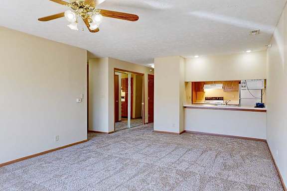A living room with a ceiling fan and carpeted floor, with a passthrough countertop to the kitchen.