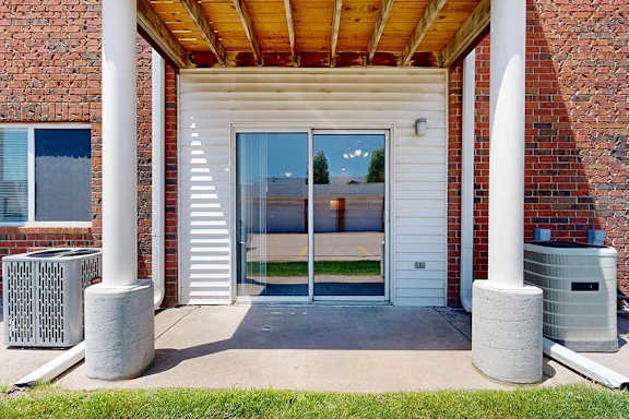 A patio with two pillars, and a sliding glass door to a living room.