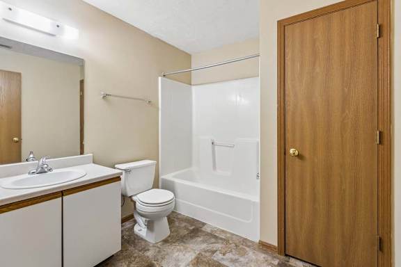Apartment bathroom with a single-sink vanity, large mirror, toilet, tub/shower combination, and durable flooring with neutral finishes throughout.