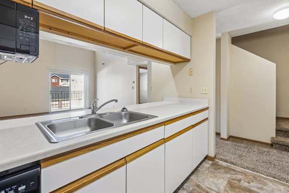 Open apartment kitchen with white cabinets, a double-basin sink, laminate countertops, and a pass-through breakfast bar overlooking the adjacent living area and staircase.