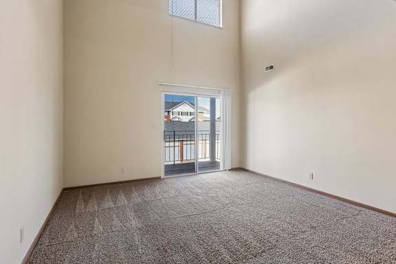 Spacious apartment living room with vaulted ceilings, neutral carpet, and a large sliding glass door with a transom window that fills the space with natural light.