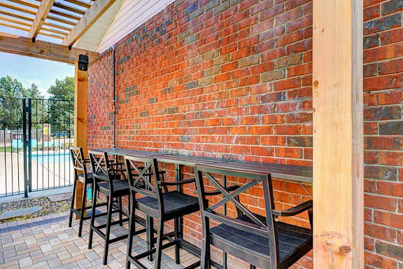A row of chairs lined up on a patio to a built-in bar top counter..