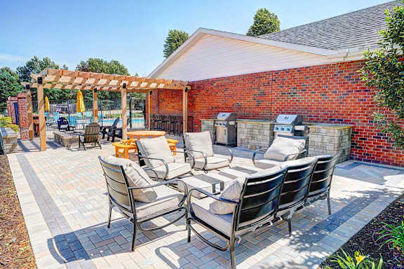 An outdoor patio with social seating areas, a picnic table, grilling stations, a fire pit, and a pergola.