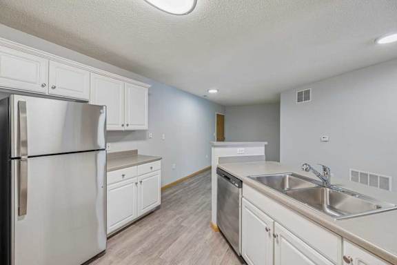 A kitchen with a refrigerator, sink, and cabinets.