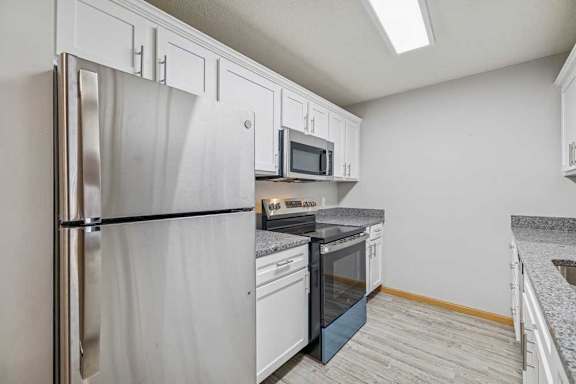 A kitchen with a refrigerator, microwave, oven, and sink.