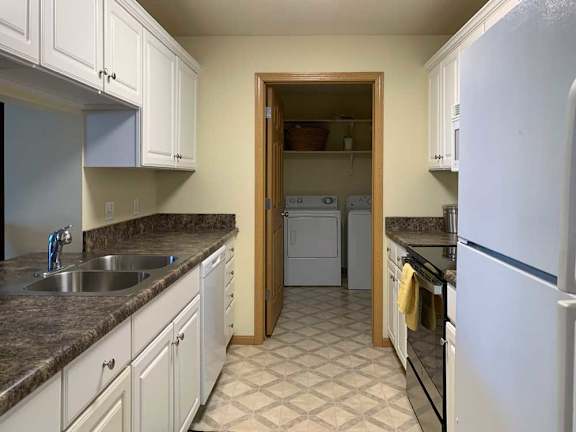 a kitchen with white cabinets, dark counter tops, vinyl flooring, and a white fridge