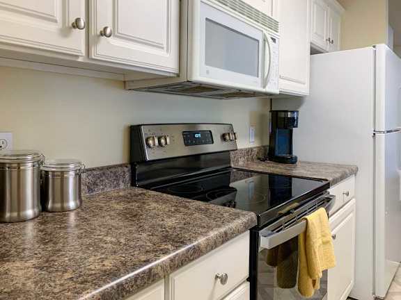 a kitchen with white cabinets, dark grey countertops, a white microwave and glass top stove