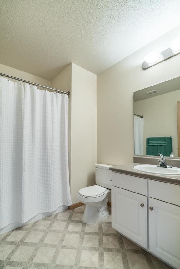 A white toilet sits in a bathroom with a white shower curtain.