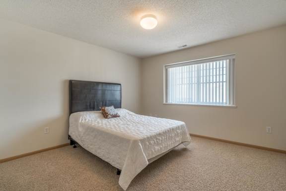 A bedroom with a bed, a window with blinds, and a wooden headboard.