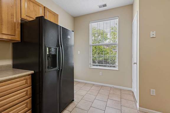 A black refrigerator in a kitchen with wooden cabinets and a window.