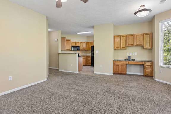 A spacious living room with a kitchenette and a ceiling fan.