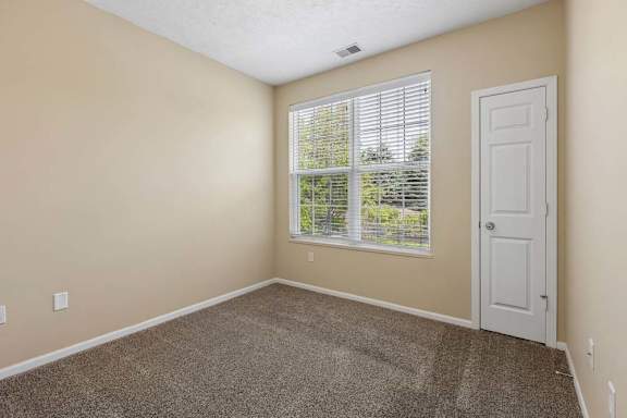 A room with a carpeted floor, a window with blinds, and a white door.
