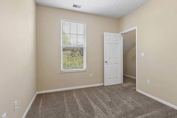 A room with a carpeted floor, a window with blinds, and a door.