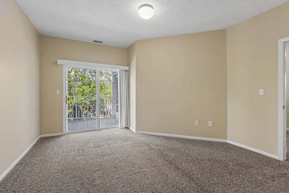A room with a carpeted floor and a sliding glass door leading outside.
