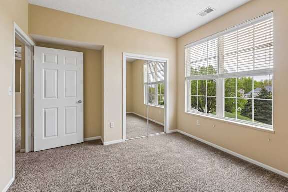A room with a white door, carpeted floor, and a window with blinds.