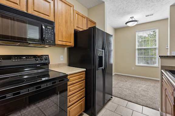 A black refrigerator is in a kitchen with wooden cabinets.