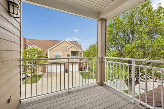 Covered apartment balcony with sliding glass doors, tan siding, white entry door, and outdoor wall light.