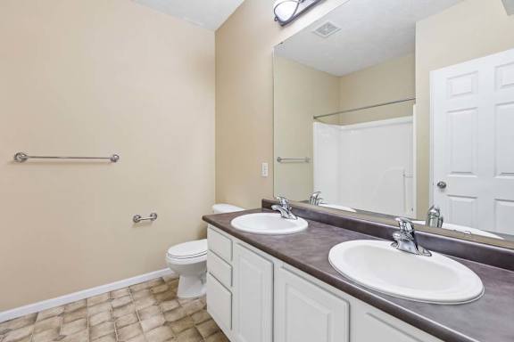 Apartment bathroom with double-sink vanity, large mirror, white cabinetry, and tub shower combo.