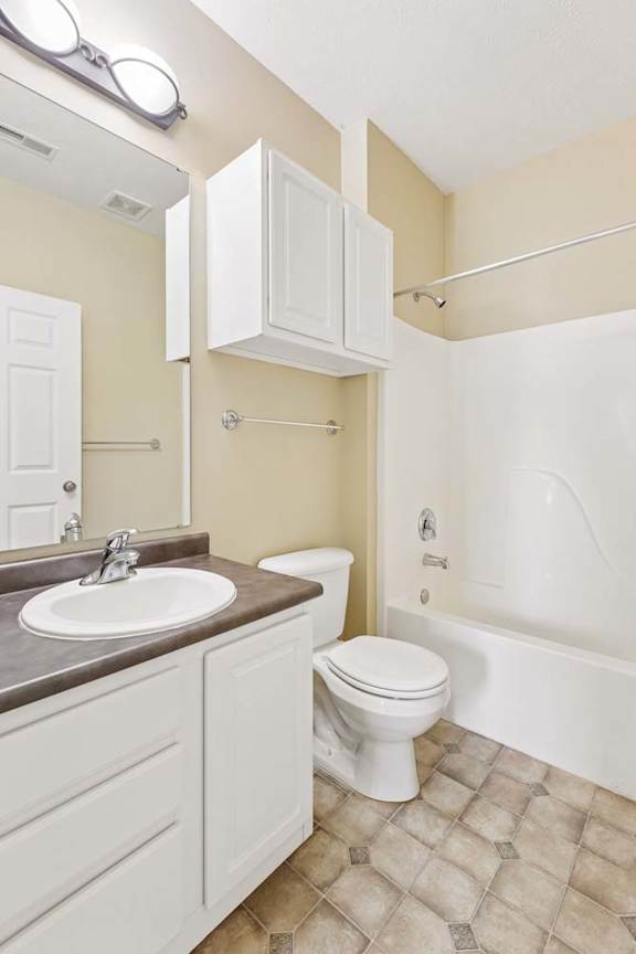 Apartment bathroom with white vanity, large mirror, tub shower combo, and patterned tile flooring.