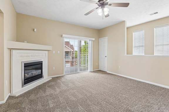 Carpeted apartment living room with fireplace, ceiling fan, sliding glass doors, and private balcony access.