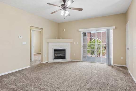 Apartment living room with carpet, fireplace, ceiling fan, and sliding glass doors leading to a balcony.