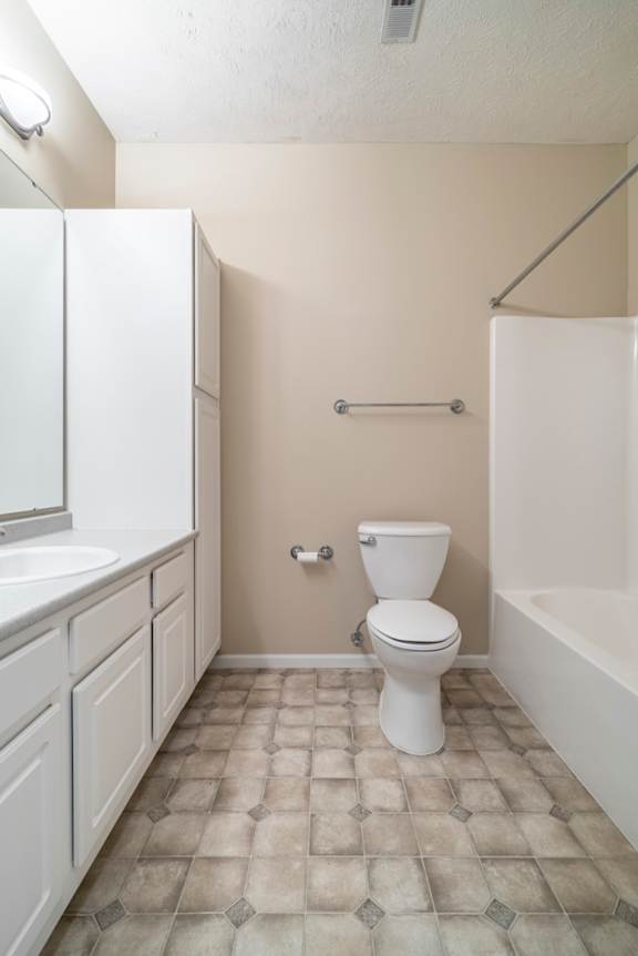 A white toilet sits in a bathroom with a white sink and a white bathtub.