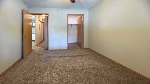 a carpeted bedroom with two doors, one open to a walk-in closet