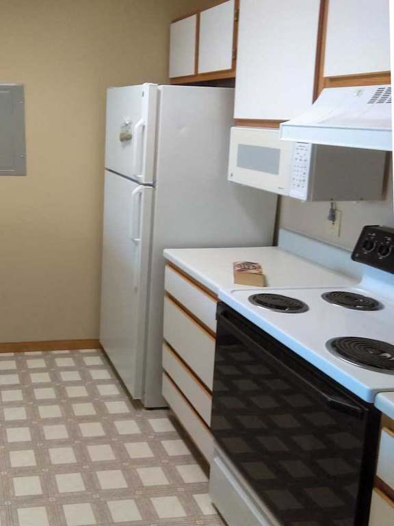 a kitchen with white appliances, white and brown cabinets, and vinyl flooring