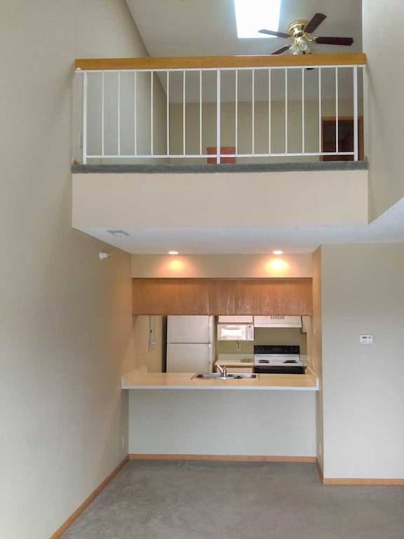 a kitchen open to the living room with a loft balcony above it