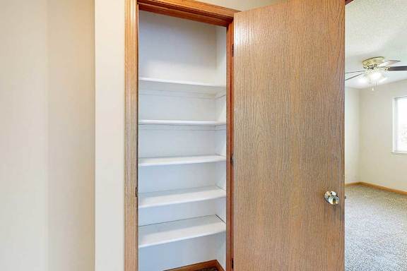 Linen closet with built-in white shelving for organized storage in the apartment hallway.