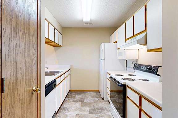 Galley-style apartment kitchen with white cabinets, laminate countertops, oven, microwave, and refrigerator.