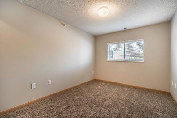 A room with a carpeted floor and a window with blinds.