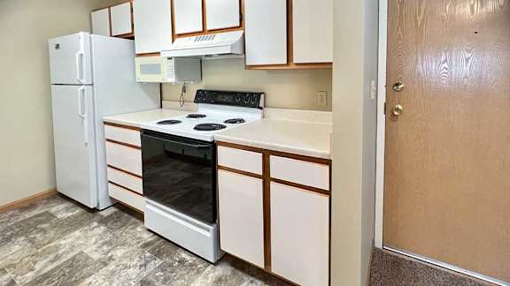 a kitchen with white appliances, white and brown cabinets, and vinyl flooring