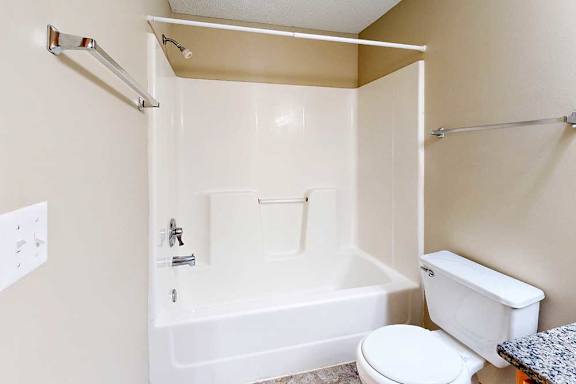 Apartment bathroom featuring a full-size tub and shower combo, neutral walls, toilet, and towel bars