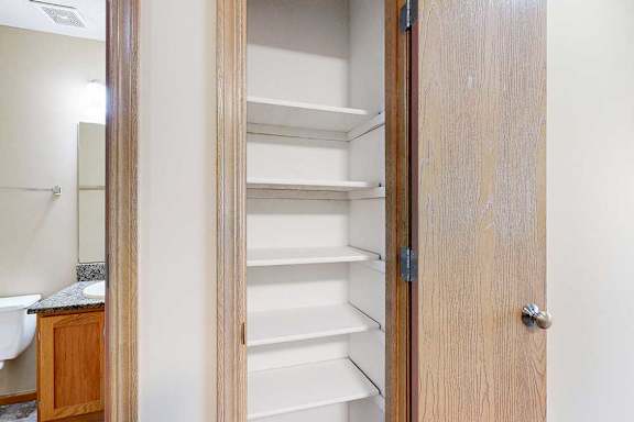 Linen closet with multiple white built-in shelves located just outside the bathroom in this apartment interior.