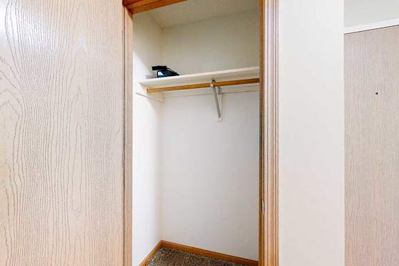 Coat closet with single hanging rod and upper shelf, wood-trimmed doorway, and carpeted flooring.