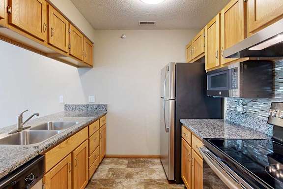 Galley-style kitchen with wood cabinets, speckled countertops, double-basin sink, and stainless-steel refrigerator and oven.