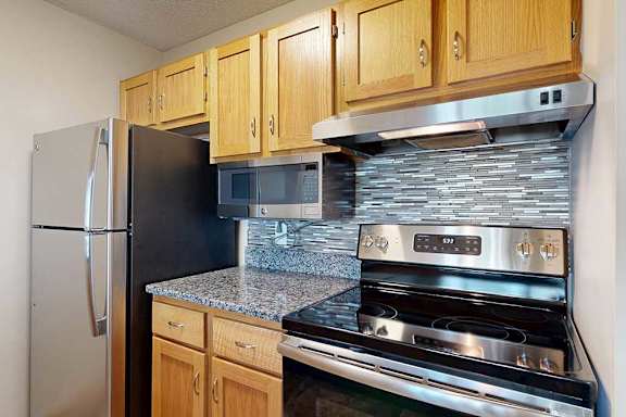 Updated kitchen with stainless-steel appliances, electric range, built-in microwave, tile backsplash, and wood cabinetry.