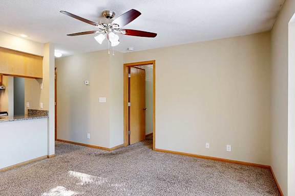 Open living and dining area with ceiling fan, neutral walls, and view toward kitchen and hallway.
