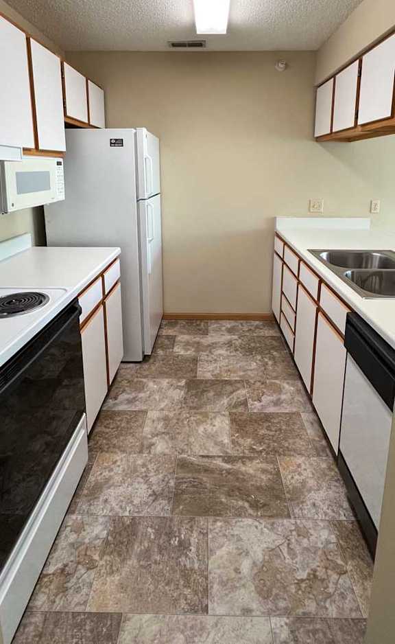 a kitchen with white and brown cabinets, white appliances, and vinyl flooring