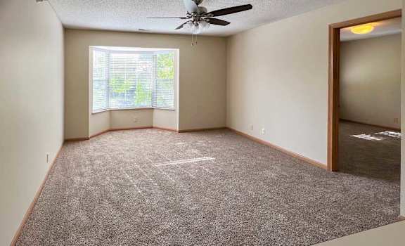a carpeted living room with a ceiling fan and a large bay-style window