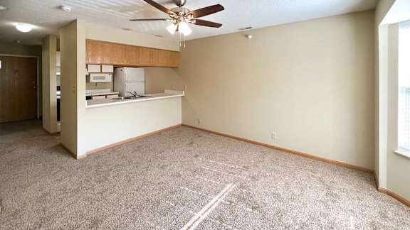 a carpeted living room with a ceiling fan, and a kitchen with a windowed countertop for dining seating