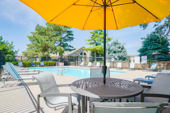 outdoor dining table and chairs shaded with a yellow umbrella next to the swimming pool