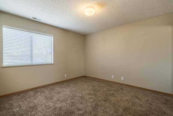 A room with a carpeted floor and a window with blinds.